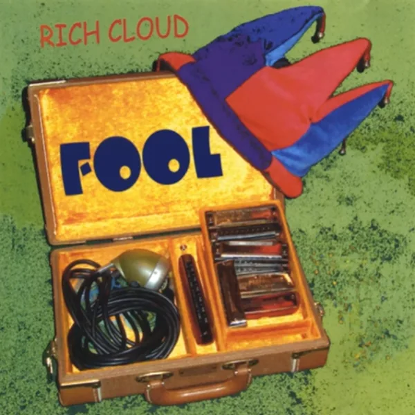 Album cover of Fool: an open harmonica case with a bullet mic, harmonicas and a jester hat on green grass